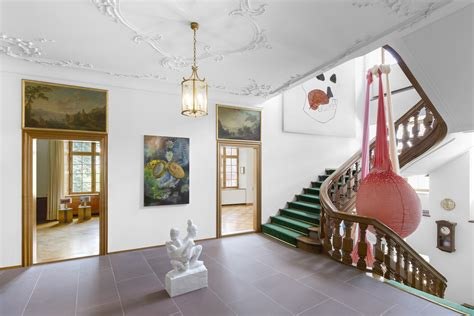 A hall of the former bank: stucco ceiling, lantern, green-carpeted stair and works hung on the walls